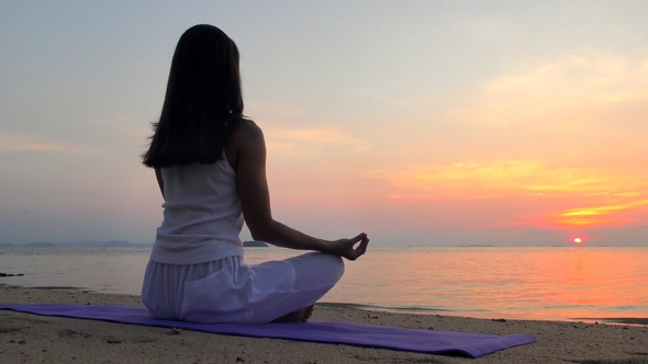 Young Woman Meditates at the Sunset Sea