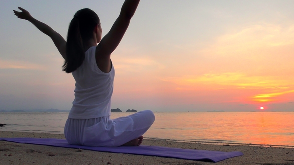 Young Woman Meditates at the Sunset Sea