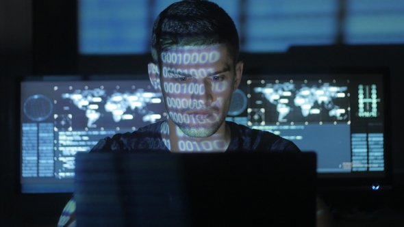 Male Hacker Programmer Working at Computer While Blue Code Characters Reflect on His Face in Cyber