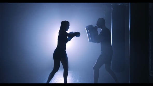 Young Woman Training with a Coach in a Boxing Club in a Smoky Gym