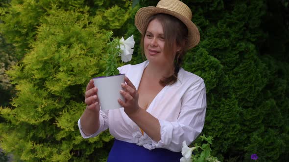 Zoom in to Happy Overweight Woman Stretching Pot with White Flower Admiring Plant in Slow Motion