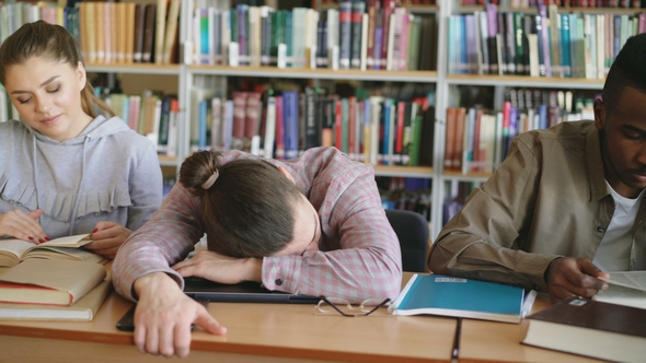 Pan Shot of Diligent Students Preparing for Exams Doing Homework and Tired Guy Sleeping on Table in