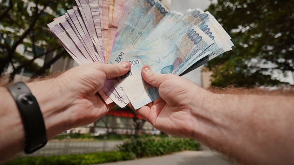 A Man Holds Philippine Money Bills in His Hands.
