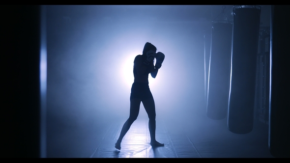Woman Sportsman Boxing in Smoky Studio Silhouette on a Dark Background