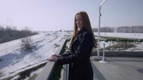 Side View Portrait of Thoughtful Young Caucasian Woman Standing on Winter Terrace on Sunny Day