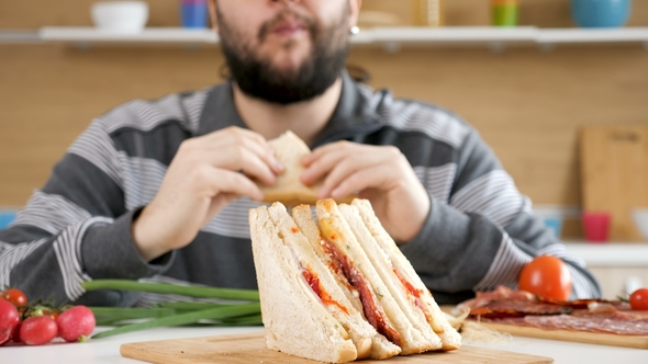 Man Entering the Kitchen, Taking a Seat and Starts Eating a Sandwich