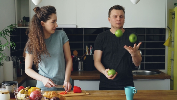 Cheerful Woman Preparing Breakfast in the Kitchen, Her Husband Comes Taking Apples