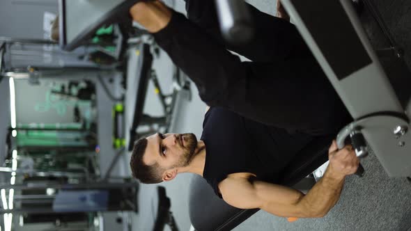 Vertical Video of Muscular Man Performs Exercises on a Sports Training Apparatus for Leg Muscles