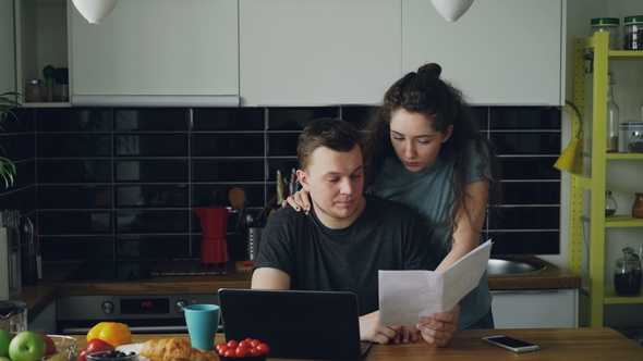 Sad Unhappy Young Man Worried About Bills Payment Using Laptop in the Kithcen at Home. His Girlfrend