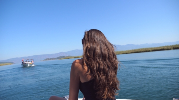 Young girl sitting on bow of boat and looking to beautiful nature landscape during summer trip