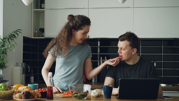 Cheerful Couple at Table Woman Dancing and Cooking While Gives Hasband To Try Red Pepper, Man