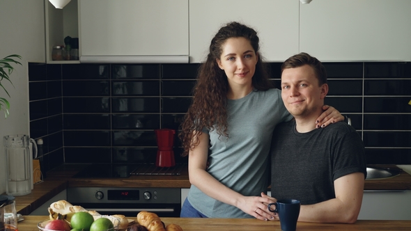 Portrait of Young Positive Smiling Caucasian Couple in Kitchen, Beautiful Woman Is Standing Near