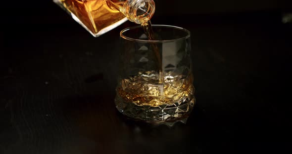 Slow Motion Golden Whiskey Pouring in the Glass with Ice Cubes From the Bottle. Close Up V3