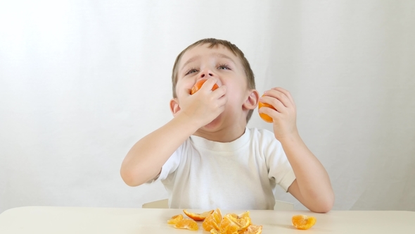 Kid Playing with Tangerines. Happy Child Sitting at Table with Hands Applying Tangerines To Eyes
