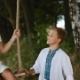 Cheerful Smiling Boy Sways His Elder Sister on a Wooden Swing, Both in Embroidered Shirts. - VideoHive Item for Sale