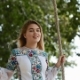 Gorgeous Blonde Girl in a Trendy, Embroidered Dress Sways on a Wooden Swing Seat in the Garden - VideoHive Item for Sale