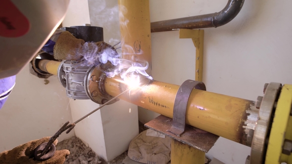 Industrial Worker Wearing Protective Equipment Welding Metal Tubes on a Plant alt