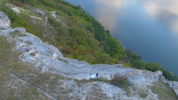 Great Sunset on the Lake Between the Mountains. A Couple Hugging at the Edge of the Cliff