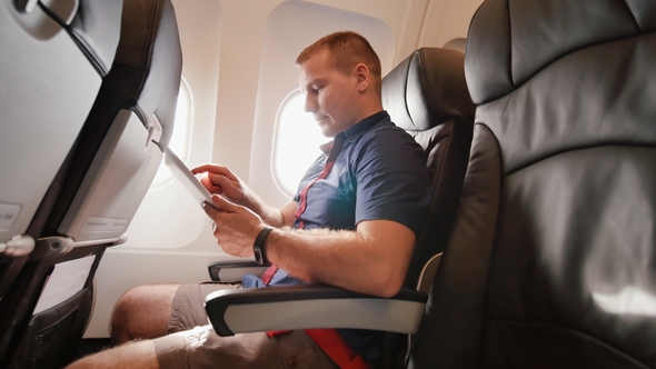 A Young Tourist on the Plane Works with the Tablet Before Leaving