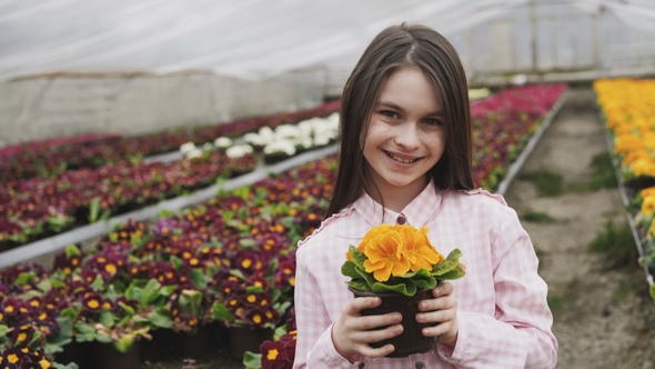 Portrait of Happy Young Girl Smelling Flowers in Greenhouse at Camera