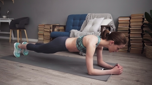Fitness Woman Using Smartphone and Doing Plank Exercise at Home