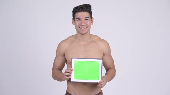 Happy Young Shirtless Muscular Man Thinking While Showing Digital Tablet