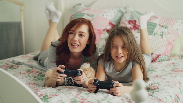 Beautiful Happy Mother with Little Daughter Laughing and Have Fun While Playing Computer Console
