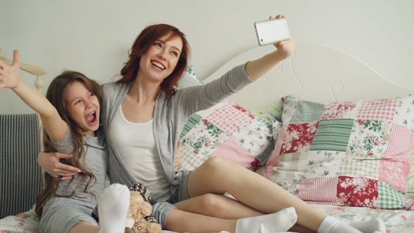 Happy Mother and Little Girl Taking Selfie Photo with Smartphone Camera and Have Fun Grimacing While