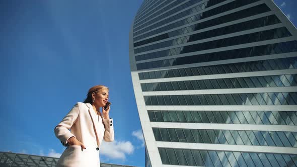 Beautiful Young Business Woman Calling By Phone on the Background of Skyscrapers