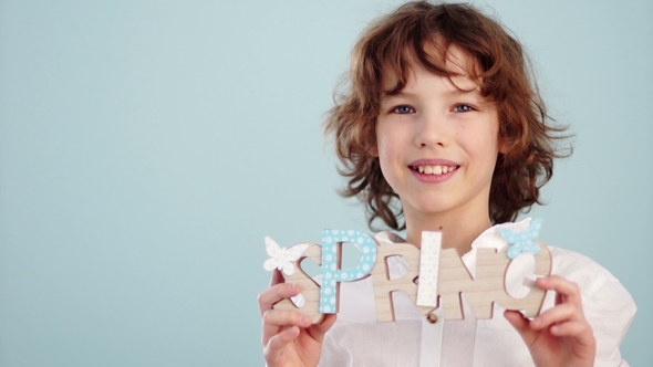 A Red-haired, Curly-haired Boy in a White Shirt Is Holding a Spring Decor Portrait in Studio