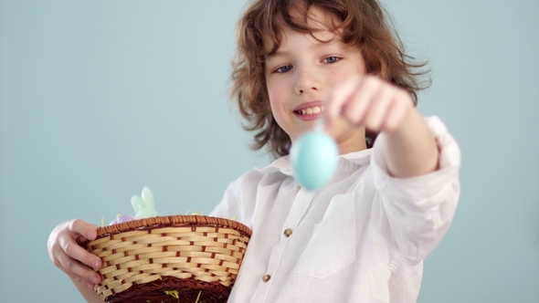 Boy with Easter Basket. Teenager Shows on His Outstretched Hand a Gently Blue Easter Egg