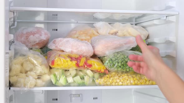 Female Hands pulls frozen meat out of the fridge. Frozen fruits, vegetables