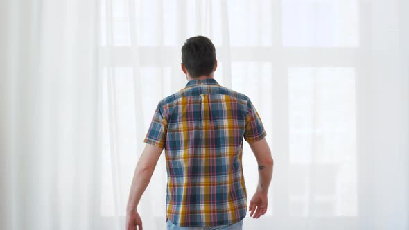 Young Man Opening Window Curtain at Home