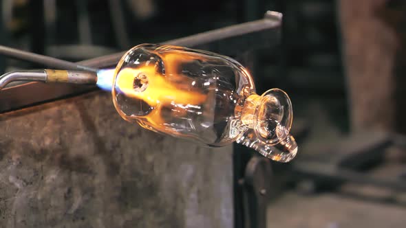 Glass artist rotates vase while heating it with blowtorch. Close up.