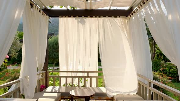 Outdoor wooden gazebo with white curtains.