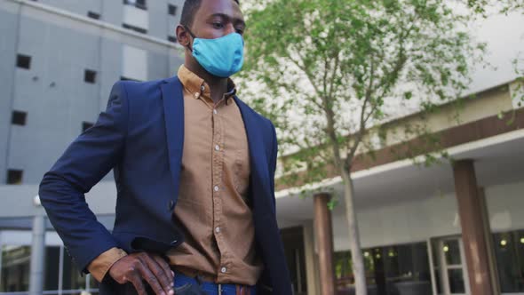 African american businessman wearing face mask using smartphone in street
