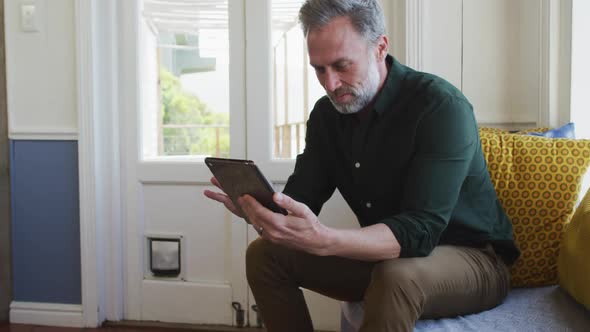 Happy caucasian mature man siting in living room and using tablet