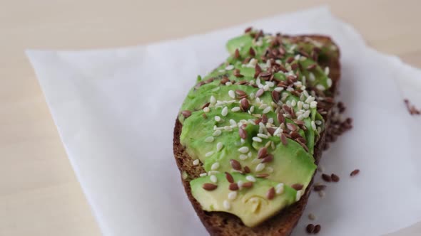 Healthy avocado toast rotating on wooden board. Sesame and flax seeds. Vegetarian food.