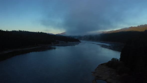 Flying Over a Lake in Misty Dawn Lights in Early Morning. Aerial View