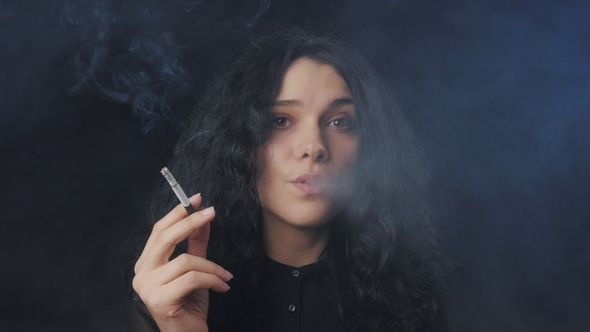 Young Brunette Woman with Curly Hair Is Smoking a Cigarette and Looking at the Camera in