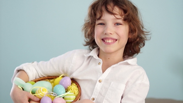 Curly Red-haired Child in a White Shirt with a Figure of an Easter Bunny and a Set of Easter Eggs in