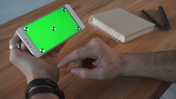 Man Using Smartphone with Green Screen at Table