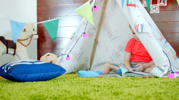 Little Boy Is Reading Book in His Self Made Wigwam in Playroom