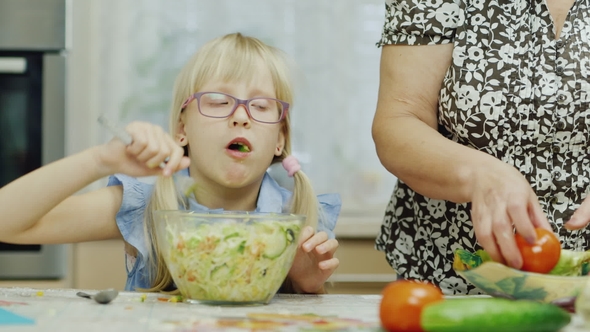 Granddaughter Visiting Grandmother. A 6 Year Old Girl Eats a Salad. Next To Her, an Elderly Woman