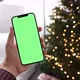 Man holding modern smartphone with green screen chromakey near Christmas tree lights on background - VideoHive Item for Sale