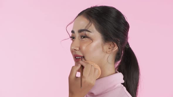 Beauty concept. The beautician is making up an Asian model on a pink background. 4k Resolution.