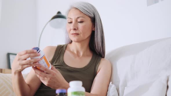 Concentrated Asian woman opening a jar of medicines