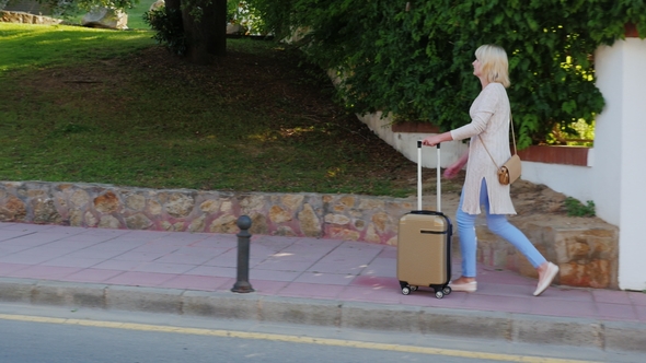 Woman with Travel Bag Goes Along the Resort Area. On a Clear Sunny Day