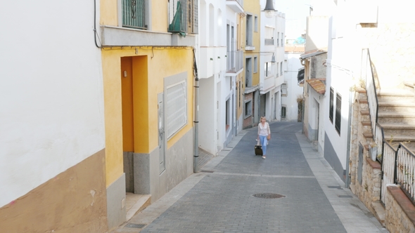 Tourist with Travel Bag Goes Up the Narrow Street of the Old European City in Spain