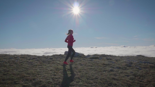 Young Woman Is Jogging in Mountains Above Clouds at Sunny Day. Sky Running